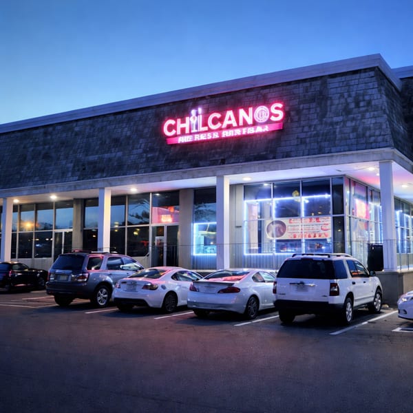 Chilcanos restaurant exterior at dusk with a bright pink neon sign and cars parked in front.