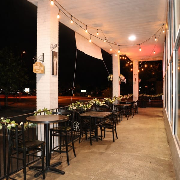 Outdoor patio at night with string lights, tables, and chairs, decorated with white flowers.