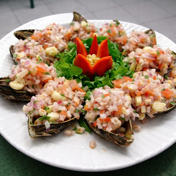 A white plate with mussels topped with ceviche, garnished with lettuce and red pepper.