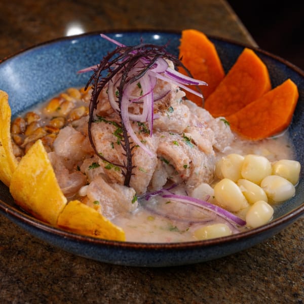 Ceviche in a blue bowl with fish, red onion, corn, sweet potato, and plantain chips.