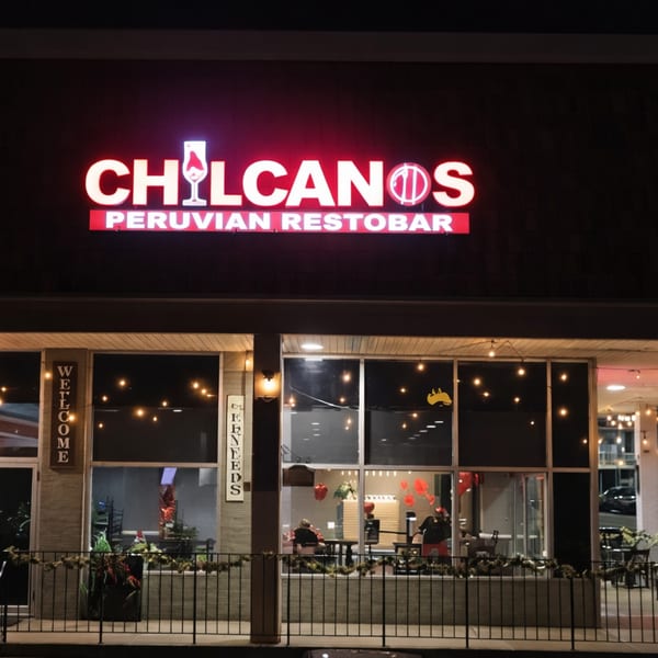 Exterior night view of Chilcanos Peruvian Restobar with a bright neon sign and string lights.