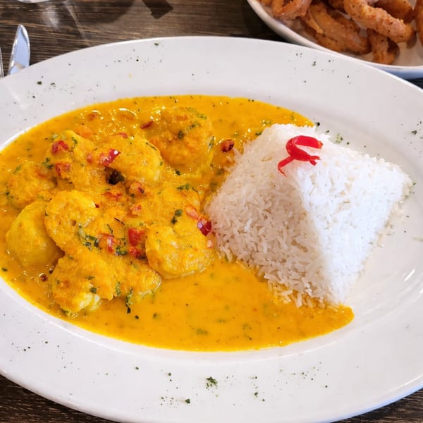 Shrimp in a vibrant yellow curry sauce with white rice and red pepper garnish on a white plate.