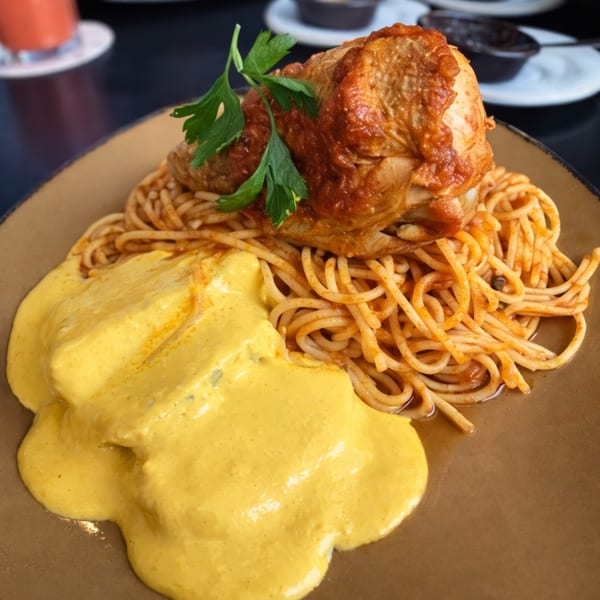 Peruvian aji de gallina with spaghetti and a chicken leg on a brown plate.